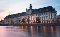 Zdjęcie gmachu głównego Uniwersytetu Wrocławskiego w promieniach zachodzącego słońca.