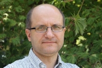 Prof. Jacek Dziubański na tle krzewów.