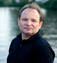 Zdjęcie en face Grzegorza Karcha na tle tafli jeziora.