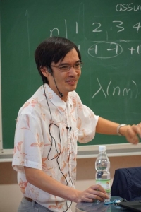 Zdjęcie uśmiechniętego Terence'a Tao na tle tablicy zrobione podczas jego wykładu na konferencji Analysis and Applications.